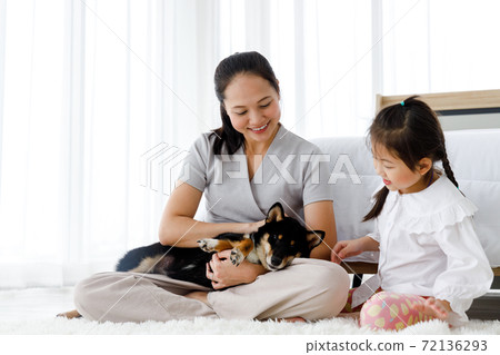 Asian mother and daughter sitting on floor with black Shiba Inu. Asian mother and daughter sitting on floor with black Shiba Inu. 72136293