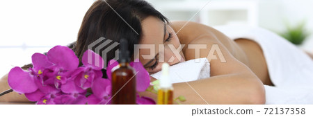 Woman lies with closed eyes on massage table in spa center 72137358