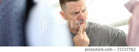 Pensive man looks at hanger with clothes. 72137762