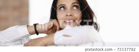Woman stands with her elbows on hanger and looks up dreamily. 72137782