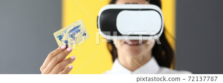 Woman is wearing virtual reality glasses in her hands she is holding bank credit card Woman is wearing virtual reality glasses in her hands she is holding bank credit card 72137787