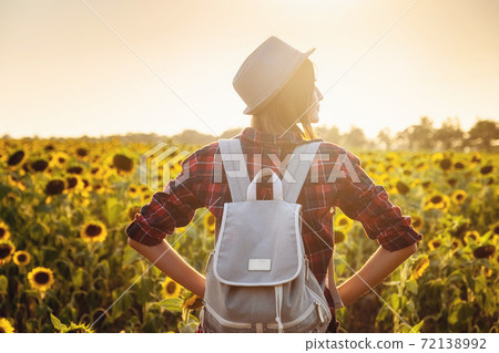 Beautiful young girl enjoying nature on the field of sunflowers at sunset 72138992