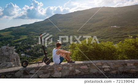 Young man riding an electric scooter on mountain range. Ecological transportation concept 72139042