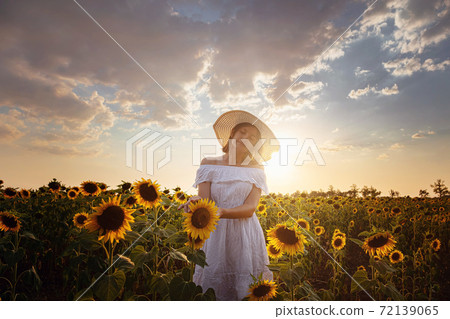 Beautiful young woman enjoying nature on the field of sunflowers at sunset Beautiful young woman enjoying nature on the field of sunflowers at sunset 72139065