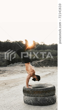 Bodybuilder in mask doing exercises for arms on tyres 72141610