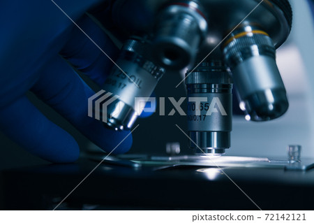 Sample slide and microscope with metal lens at laboratory. 72142121
