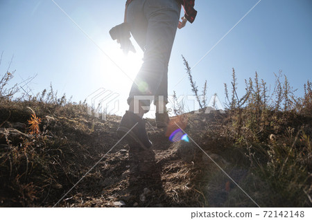 Low angle close-up woman photographer climbs the mountain in hand holding a camera. Against the backdrop of the bright sun on a sunny day Low angle close-up woman photographer climbs the mountain in hand holding a camera. Against the backdrop of the bright sun on a sunny day 72142148