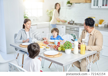 Latin family having dinner together at home. Woman serving a meal for her husband and children, standing in the kitchen 72142154
