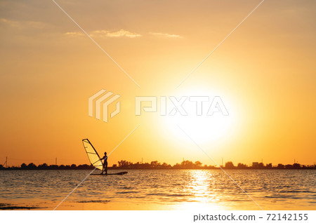Silhouette woman windsurfer on waves of the bay at beautiful sunset Silhouette woman windsurfer on waves of the bay at beautiful sunset 72142155