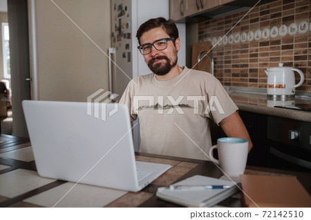 Smiling hipster freelancer holding hands behind head sitting at office desk behind laptop. 72142510