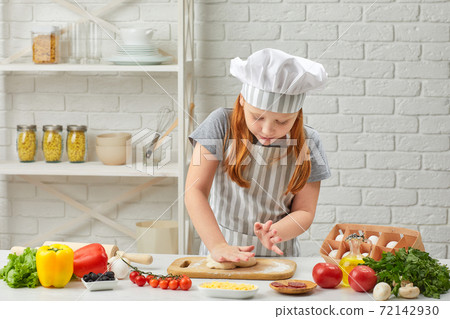 little child girl in cap and an apron knead the dough little child girl in cap and an apron knead the dough 72142930
