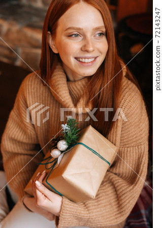 Close-up view of charming redhead young woman holding gift box in hand received for Christmas. 72143247