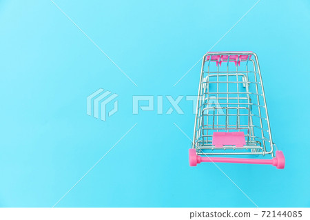 Small supermarket grocery push cart for shopping toy with wheels isolated on blue pastel colorful trendy background Copy space. Sale buy mall market shop consumer concept. Small supermarket grocery push cart for shopping toy with wheels isolated on blue pastel colorful trendy background Copy space. Sale buy mall market shop consumer concept. 72144085
