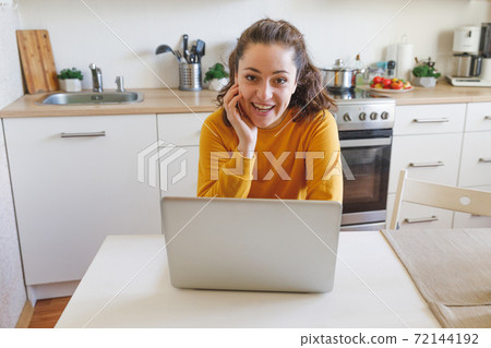 Mobile Office at home. Young woman sitting in kitchen at home working using on laptop computer. Lifestyle girl studying or working indoors. Freelance business quarantine concept. Mobile Office at home. Young woman sitting in kitchen at home working using on laptop computer. Lifestyle girl studying or working indoors. Freelance business quarantine concept. 72144192