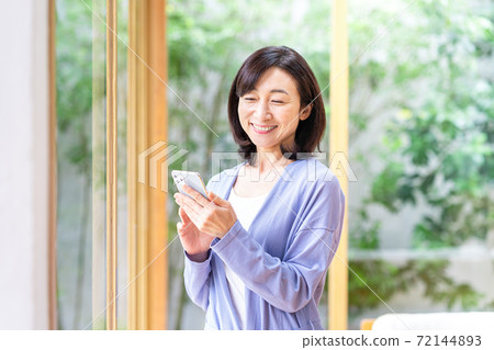 A middle woman who operates a smartphone in the living room A middle woman who operates a smartphone in the living room 72144893