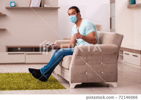 Young man watching tv at home during pandemic 72146066