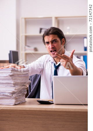 Young male employee unhappy with excessive work in the office 72147342