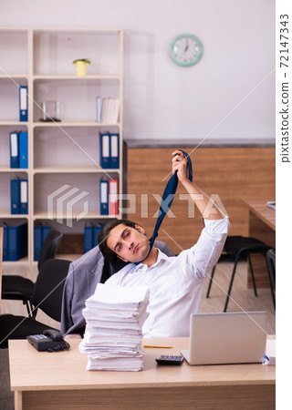 Young male employee unhappy with excessive work in the office Young male employee unhappy with excessive work in the office 72147343