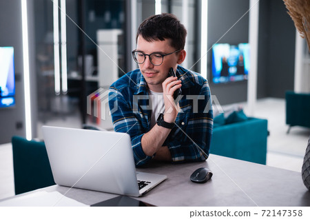 View of concentrated talented skilled male focused on screen of laptop computer, reads necessary information for creating budget report 72147358