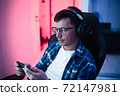 Image of caucasian youngman in headphones using cellphone playing video game in a gaming chair at home 72147981