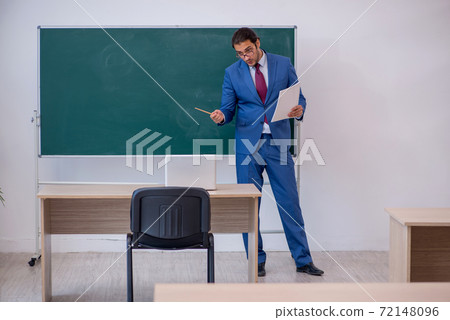 Young male teacher in suit in front of green board 72148096