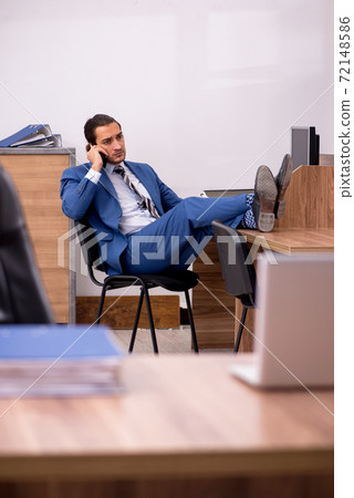 Young male employee sitting at workplace Young male employee sitting at workplace 72148586