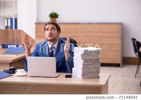 Young male employee unhappy with excessive work in the office Young male employee unhappy with excessive work in the office 72148645