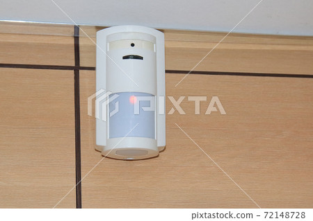Motion sensor of the security alarm system. A white volume sensor hangs on the wall in a room or Motion sensor of the security alarm system. A white volume sensor hangs on the wall in a room or 72148728