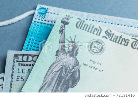 A US stimulus check on with some one-hundred-dollar bills and a medical mask 72151410