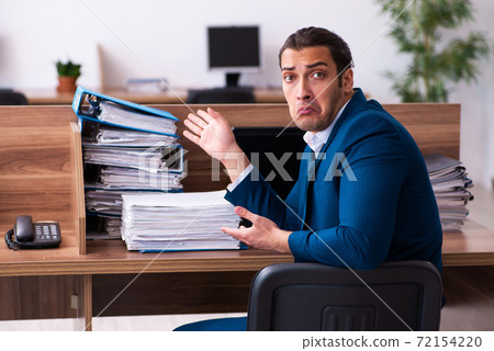 Young male employee unhappy with excessive work in the office Young male employee unhappy with excessive work in the office 72154220
