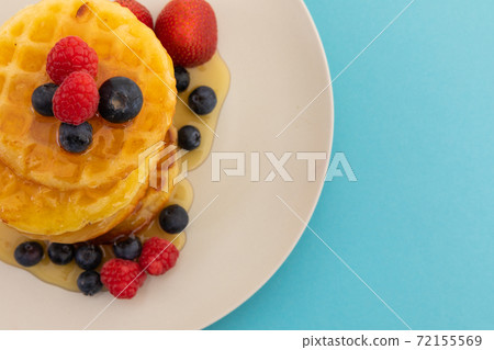 Stack of pancakes with berries and honey on plate on blue background 72155569