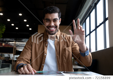 Smiling mixed race businessman waving on video call in creative office Smiling mixed race businessman waving on video call in creative office 72156899