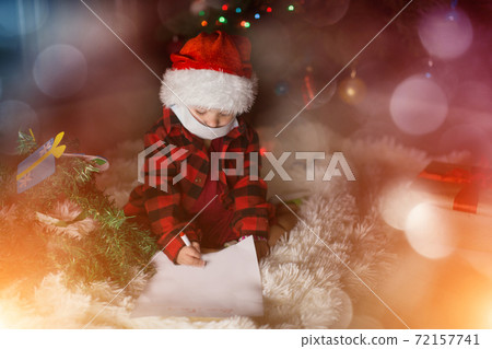 a child in red clothes and medical mask is sitting waiting for the new year. the concept of celebrating Christmas at midnight. holiday costume. a girl writes a letter to Santa Claus. wish list 72157741