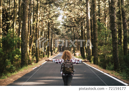Success and feedom concept with woman and backpack viewed from back and long asphalt road staight in the middle of a high trees nature forest - life after coronavirus lockdown Success and feedom concept with woman and backpack viewed from back and long asphalt road staight in the middle of a high trees nature forest - life after coronavirus lockdown 72159177
