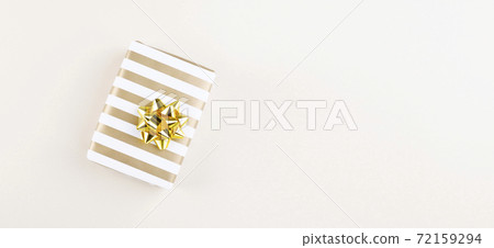 Gift in striped paper with golden bow on beige background. Top view. Copy space 72159294