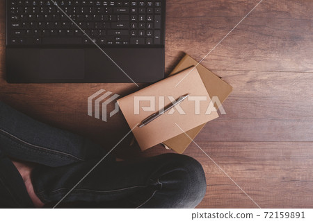 Top view of pen on notebook with laptop and woman's lap on wooden floor. Top view of pen on notebook with laptop and woman's lap on wooden floor. 72159891