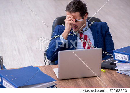 Chained male employee unhappy with excessive work in the office Chained male employee unhappy with excessive work in the office 72162850