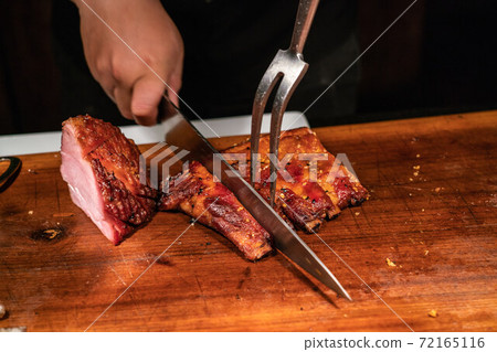 Man hand cutting baked ham and grilled ribs 72165116