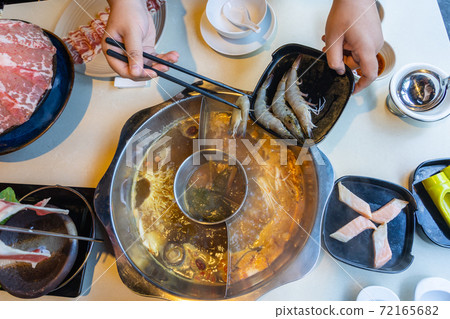 High angle view of human hand putting shrimp into the hotpot High angle view of human hand putting shrimp into the hotpot 72165682