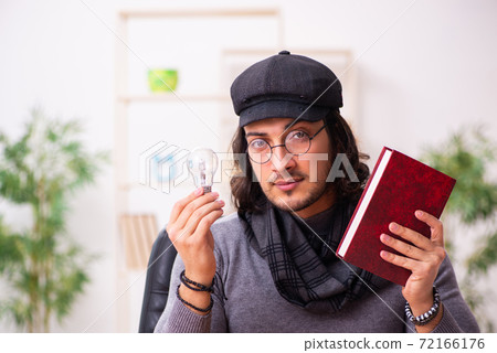Young male writer holding lamp and book 72166176