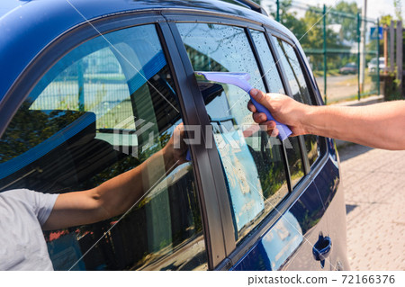 The man takes the remnants of water from the glass after washing the car at the self-service car wash, the car is blue. The man takes the remnants of water from the glass after washing the car at the self-service car wash, the car is blue. 72166376