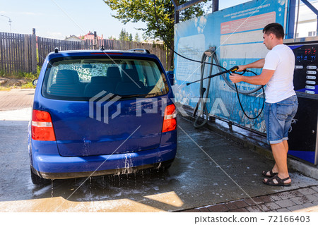 Self-service car wash, a person washes the foam from the car with water under high pressure. Self-service car wash, a person washes the foam from the car with water under high pressure. 72166403