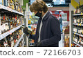 Handsome man choosing wine in the supermarket 72166703