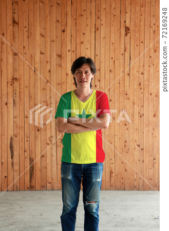 Man wearing Senegal flag color shirt and cross one's arm on wooden wall background. Man wearing Senegal flag color shirt and cross one's arm on wooden wall background. 72169248