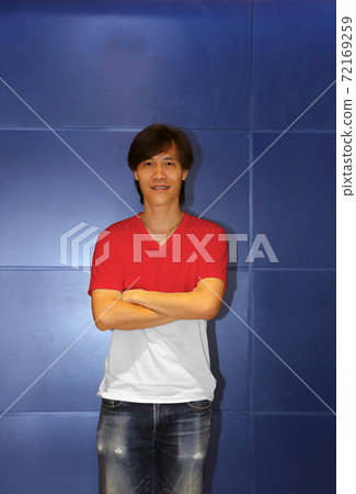 Man wearing Indonesia flag pattern shirt and cross one's arm on the blue wall background, Man wearing Indonesia flag pattern shirt and cross one's arm on the blue wall background, 72169259