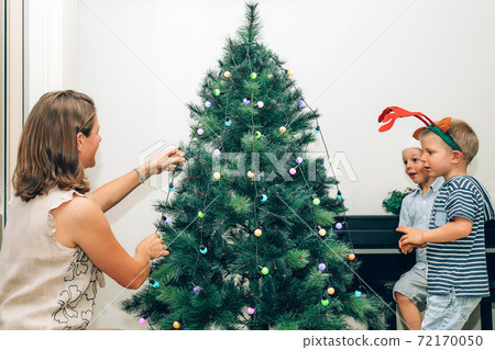 Mother with two little kids decorating Christmas tree Mother with two little kids decorating Christmas tree 72170050