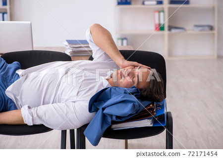 Young male employee sleeping in the office on chairs Young male employee sleeping in the office on chairs 72171454