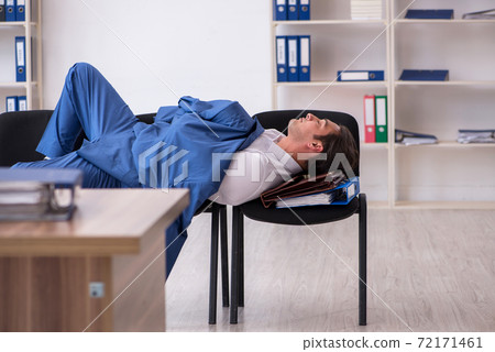 Young male employee sleeping in the office on chairs Young male employee sleeping in the office on chairs 72171461