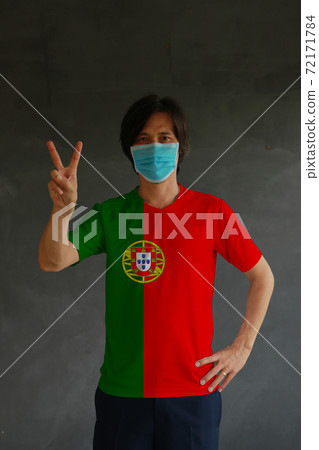 Man wearing hygienic mask and wearing Portuguese flag colored shirt and raising two fingers up Man wearing hygienic mask and wearing Portuguese flag colored shirt and raising two fingers up 72171784