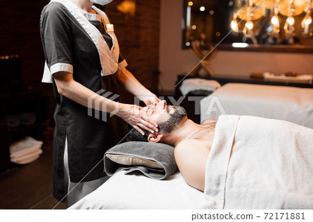 Female masseur doing facial massage to a male client Female masseur doing facial massage to a male client 72171881